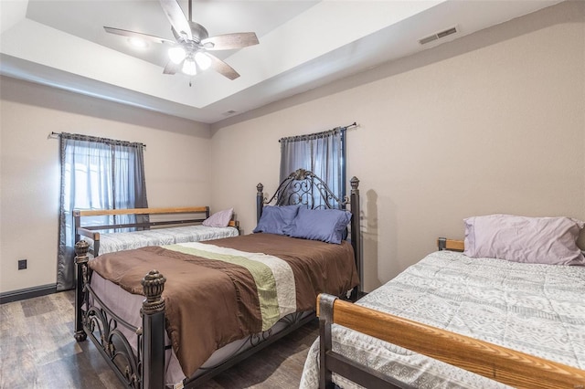 bedroom with hardwood / wood-style floors, a raised ceiling, and ceiling fan