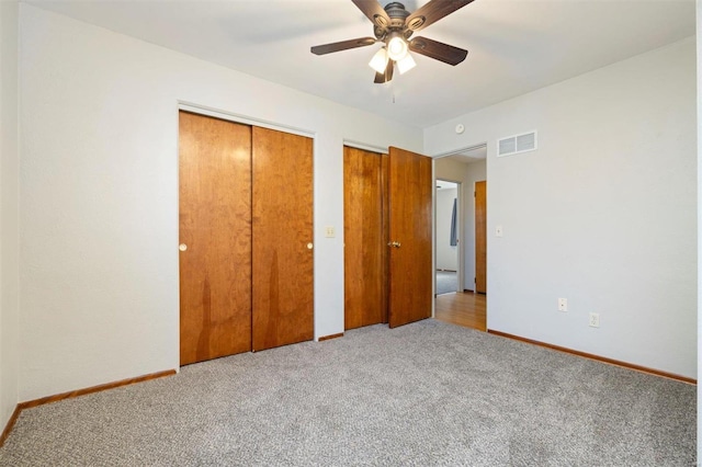 unfurnished bedroom with light carpet, two closets, and ceiling fan