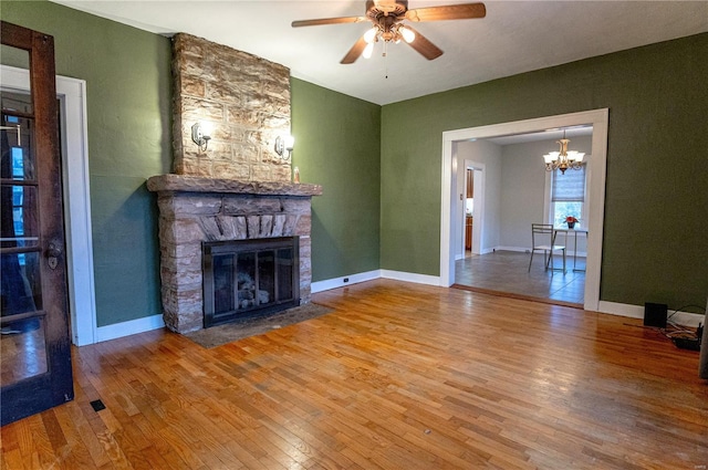 unfurnished living room featuring hardwood / wood-style flooring, a stone fireplace, and ceiling fan with notable chandelier