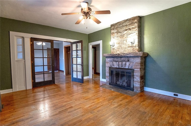 unfurnished living room with french doors, ceiling fan, a stone fireplace, and hardwood / wood-style floors