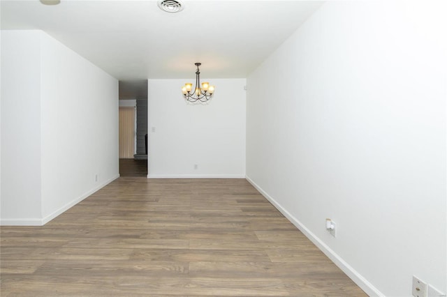 empty room with wood-type flooring and a chandelier