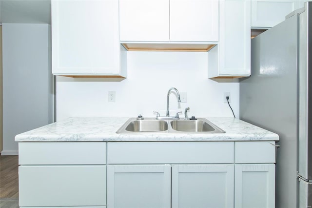 kitchen featuring wood finished floors, light stone counters, a sink, and freestanding refrigerator