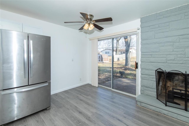 interior space featuring ceiling fan, a stone fireplace, wood finished floors, baseboards, and freestanding refrigerator