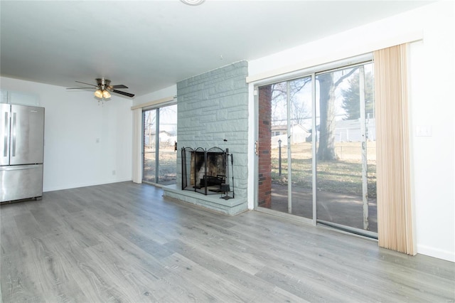 unfurnished living room with a healthy amount of sunlight, a ceiling fan, wood finished floors, and a stone fireplace