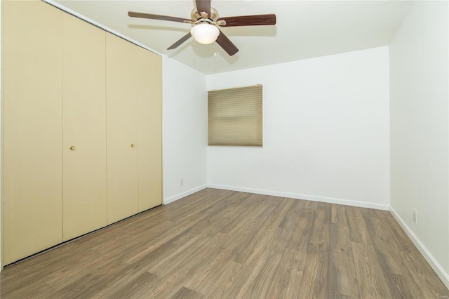 unfurnished bedroom with a closet, wood finished floors, a ceiling fan, and baseboards