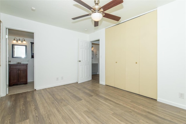 unfurnished bedroom featuring a closet, a ceiling fan, ensuite bath, wood finished floors, and baseboards