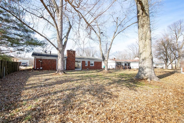 back of house featuring brick siding, a chimney, fence, and a lawn