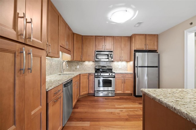 kitchen featuring light stone counters, appliances with stainless steel finishes, sink, and light hardwood / wood-style flooring