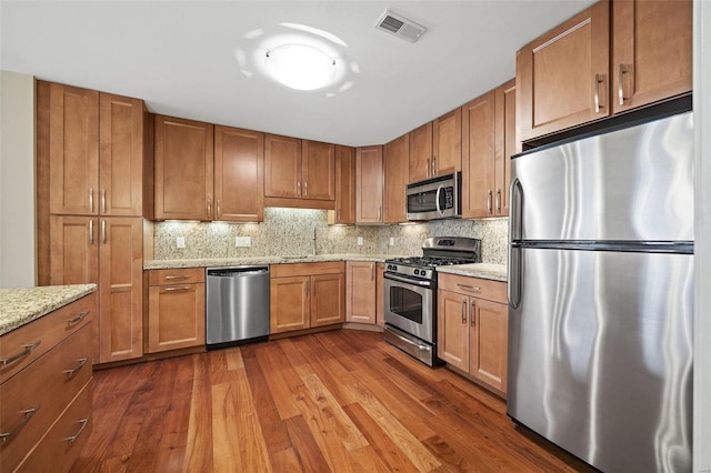 kitchen with sink, appliances with stainless steel finishes, light stone counters, dark hardwood / wood-style flooring, and decorative backsplash