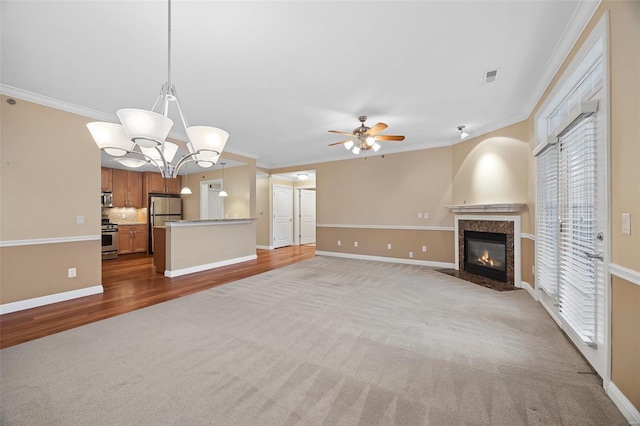 unfurnished living room featuring light carpet, a fireplace, crown molding, and ceiling fan with notable chandelier