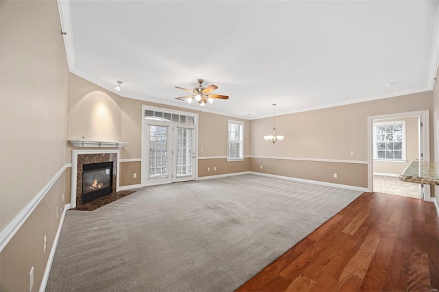 unfurnished living room featuring ceiling fan with notable chandelier, a high end fireplace, ornamental molding, and carpet flooring