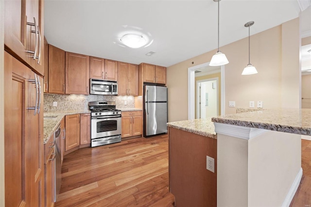 kitchen with hanging light fixtures, light hardwood / wood-style flooring, appliances with stainless steel finishes, kitchen peninsula, and light stone countertops