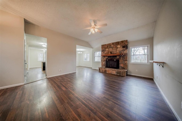 unfurnished living room with ceiling fan with notable chandelier, a fireplace, lofted ceiling, dark hardwood / wood-style flooring, and a textured ceiling