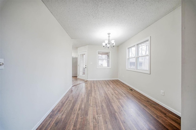 spare room with dark wood-type flooring, a chandelier, and a textured ceiling