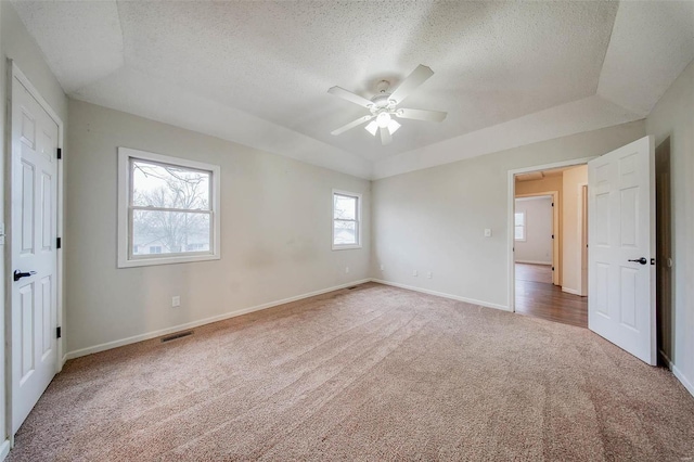 unfurnished bedroom featuring ceiling fan, a raised ceiling, a textured ceiling, and carpet