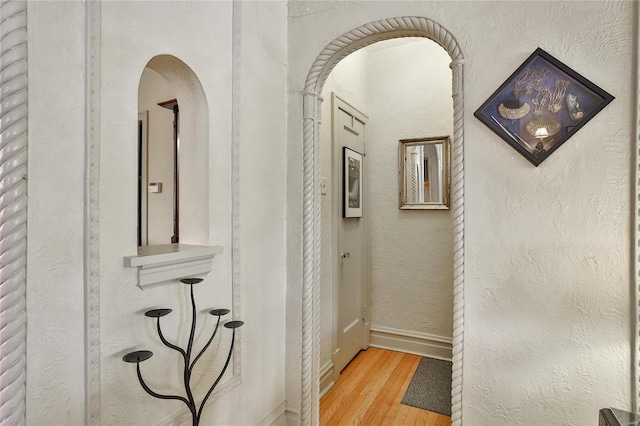 hallway featuring baseboards, arched walkways, wood finished floors, and a textured wall