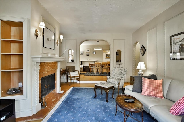 living area with a warm lit fireplace, a textured ceiling, arched walkways, and wood finished floors