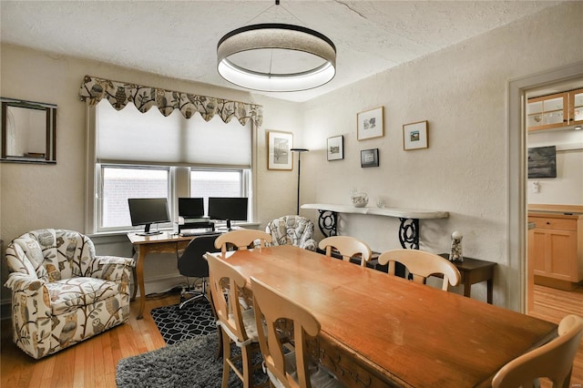 dining area with wood-type flooring, a textured ceiling, and a textured wall