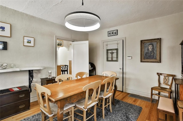 dining area featuring wood-type flooring, a textured ceiling, and baseboards