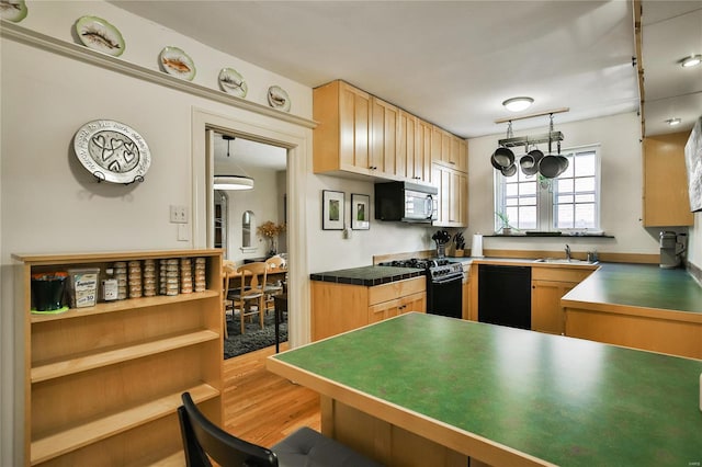 kitchen featuring black dishwasher, stainless steel microwave, wood finished floors, gas range oven, and a sink