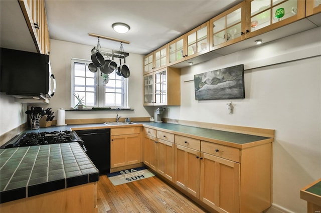 kitchen with tile counters, light wood-style floors, glass insert cabinets, a sink, and black appliances