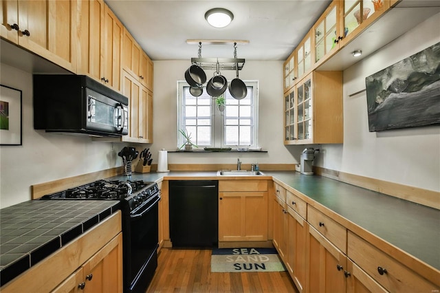 kitchen with glass insert cabinets, a sink, black appliances, and wood finished floors