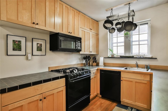 kitchen with tile countertops, light wood finished floors, light brown cabinetry, a sink, and black appliances