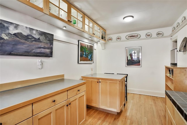 kitchen featuring baseboards, glass insert cabinets, light brown cabinetry, light wood-style floors, and open shelves