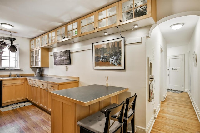 kitchen featuring light wood-style flooring, stainless steel countertops, a sink, a kitchen bar, and glass insert cabinets