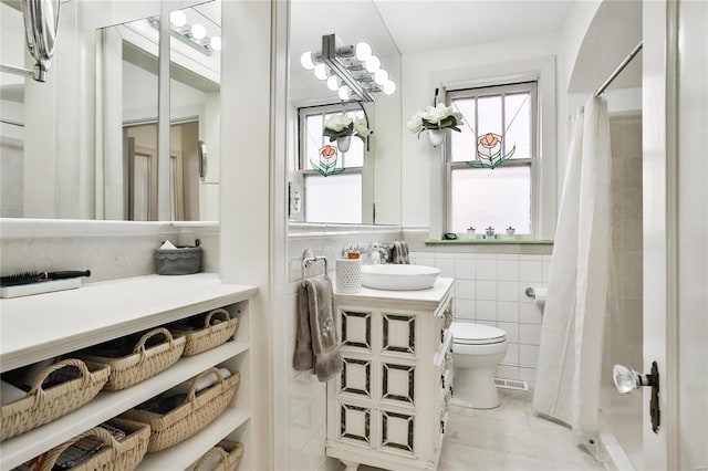 bathroom featuring toilet, a wainscoted wall, tile patterned flooring, vanity, and tile walls