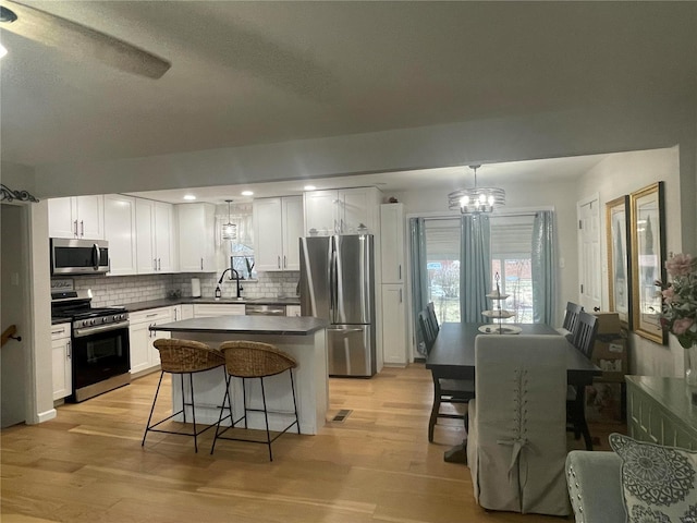 kitchen with appliances with stainless steel finishes, white cabinetry, sink, hanging light fixtures, and light wood-type flooring