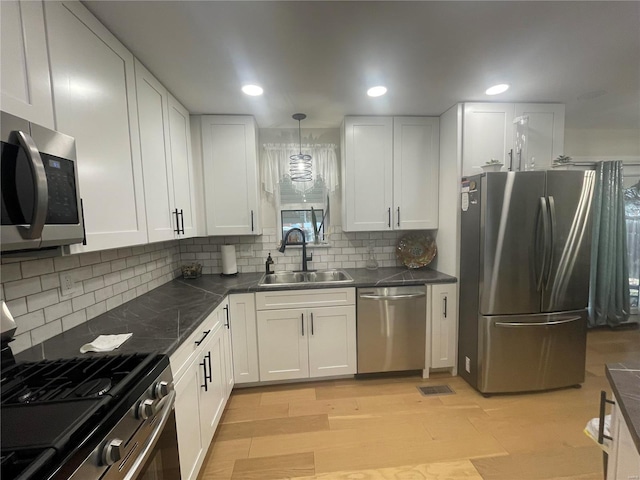 kitchen featuring tasteful backsplash, white cabinetry, sink, hanging light fixtures, and stainless steel appliances