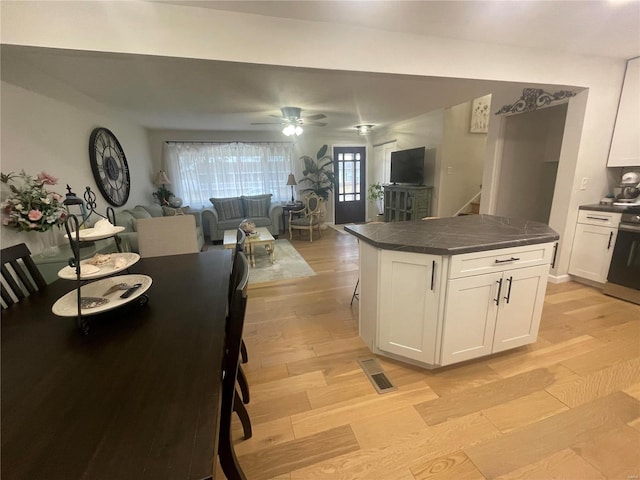 kitchen with a breakfast bar, white cabinets, a center island, ceiling fan, and light hardwood / wood-style floors