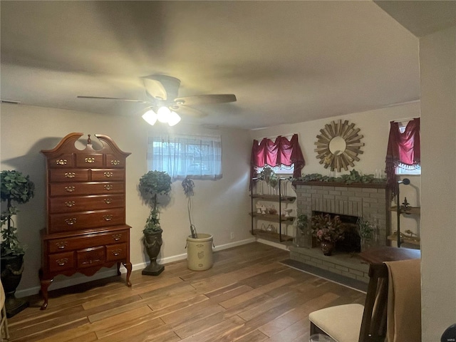 sitting room with a brick fireplace, hardwood / wood-style flooring, and ceiling fan