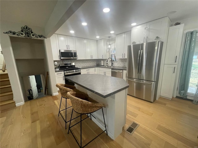 kitchen with a breakfast bar, white cabinetry, light hardwood / wood-style flooring, a kitchen island, and stainless steel appliances