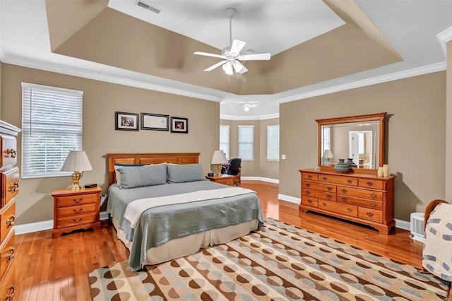 bedroom with multiple windows, light hardwood / wood-style flooring, and a tray ceiling