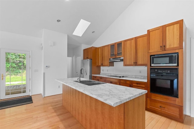 kitchen with sink, a skylight, black appliances, a center island with sink, and light wood-type flooring