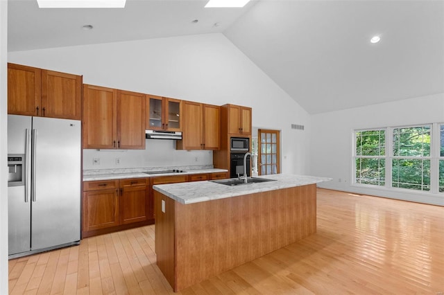 kitchen featuring built in microwave, sink, a skylight, stainless steel fridge, and a kitchen island with sink