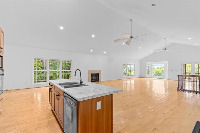 kitchen with sink, dishwasher, a kitchen island with sink, a tiled fireplace, and light wood-type flooring