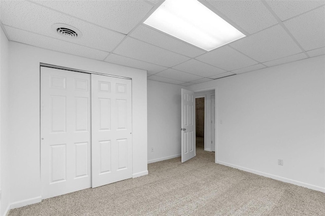 unfurnished bedroom with a paneled ceiling, light colored carpet, and a closet