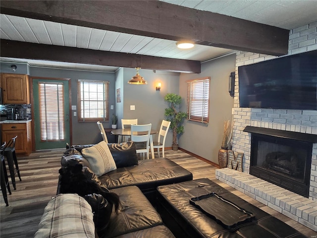 living area featuring a brick fireplace, baseboards, beamed ceiling, and wood finished floors