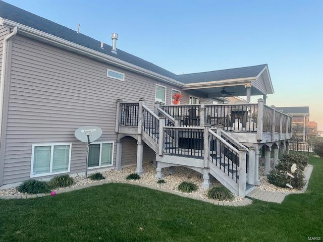 back house at dusk with a wooden deck, ceiling fan, and a lawn