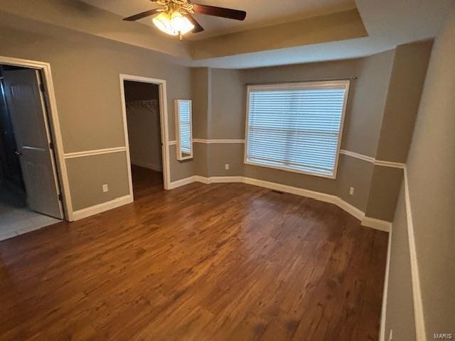 unfurnished bedroom featuring ceiling fan, a walk in closet, a tray ceiling, and dark hardwood / wood-style flooring