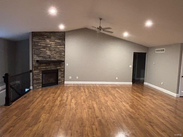 unfurnished living room featuring lofted ceiling, hardwood / wood-style floors, a stone fireplace, and ceiling fan