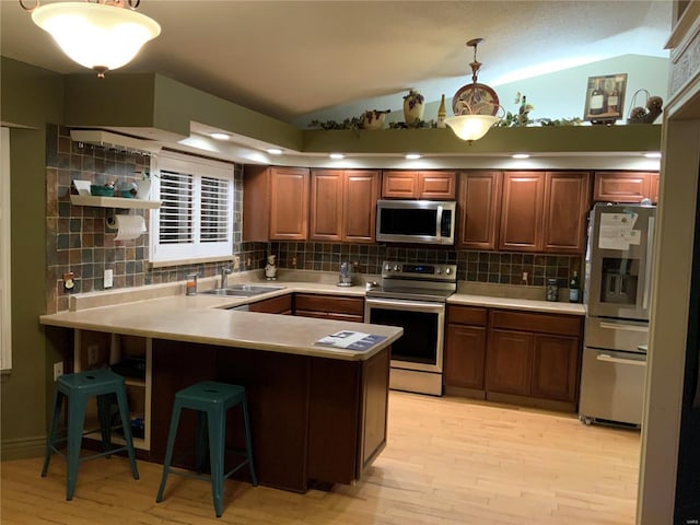 kitchen featuring sink, stainless steel appliances, decorative light fixtures, vaulted ceiling, and kitchen peninsula