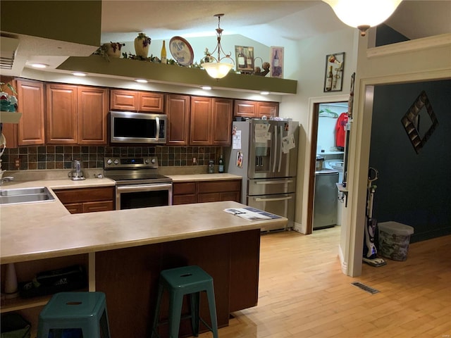 kitchen with sink, a breakfast bar, appliances with stainless steel finishes, hanging light fixtures, and decorative backsplash