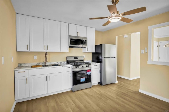 kitchen featuring appliances with stainless steel finishes, sink, white cabinets, ceiling fan, and light wood-type flooring