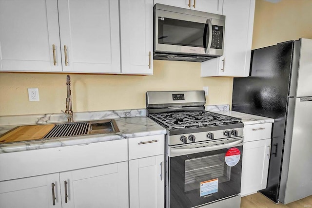 kitchen featuring appliances with stainless steel finishes, sink, white cabinets, light stone counters, and light wood-type flooring