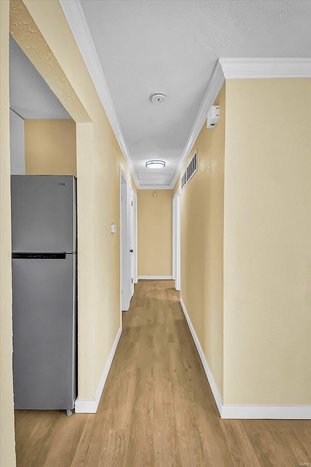 hallway with ornamental molding and light hardwood / wood-style flooring