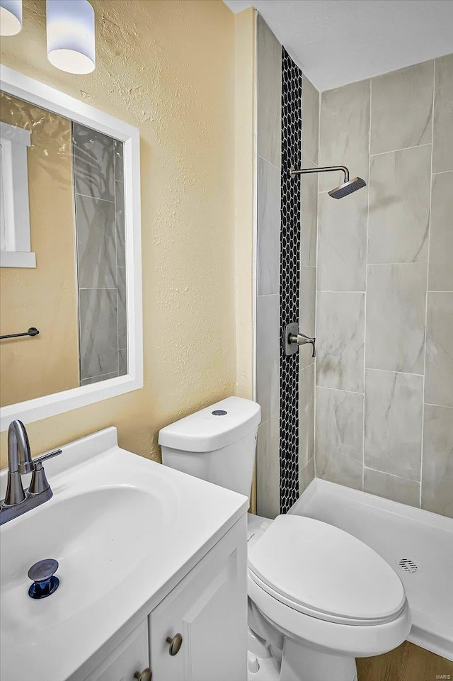 bathroom featuring vanity, toilet, and a tile shower